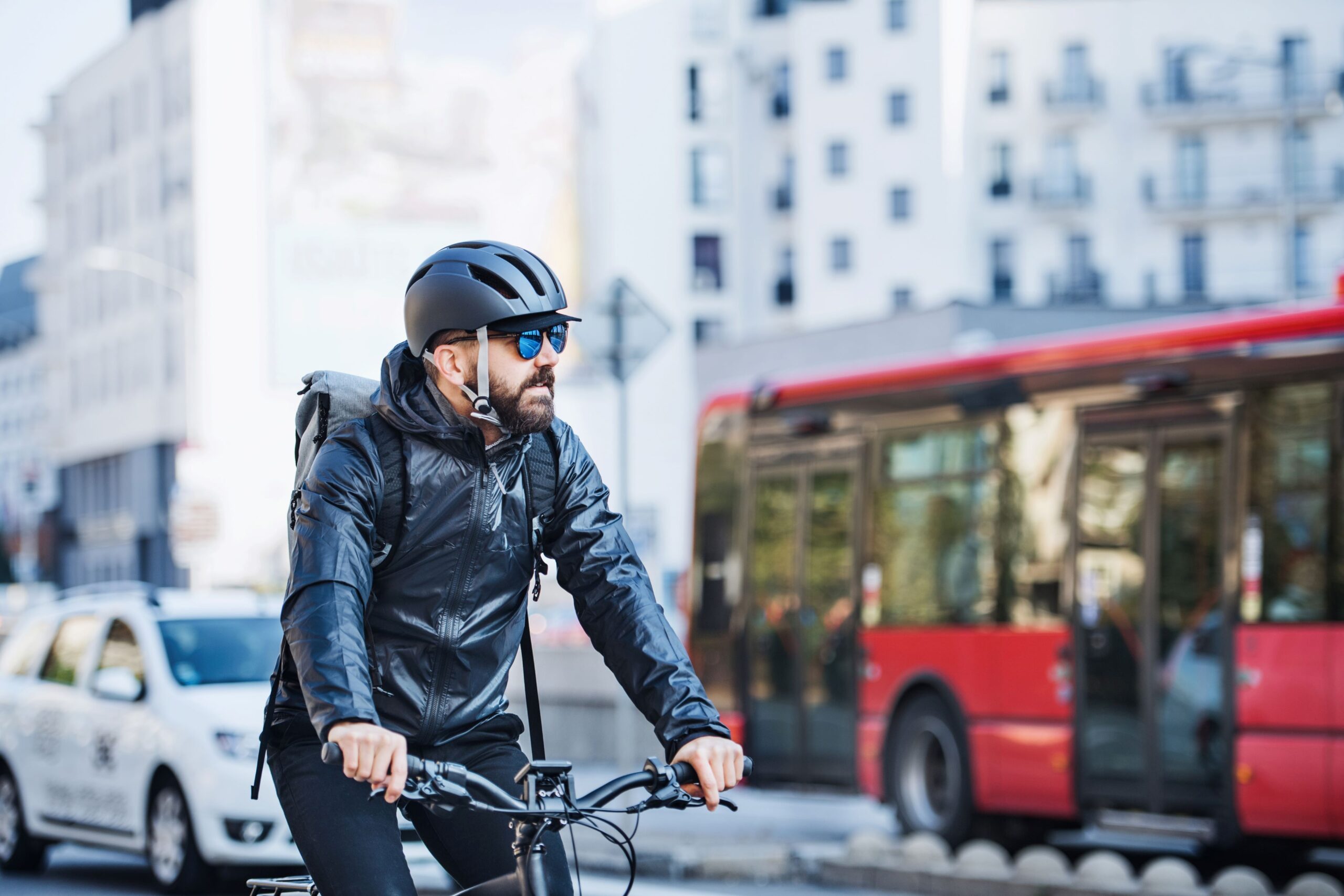 Foto de ciclista em rua de cidade sustentável, com carro e ônibus coletivo na pista