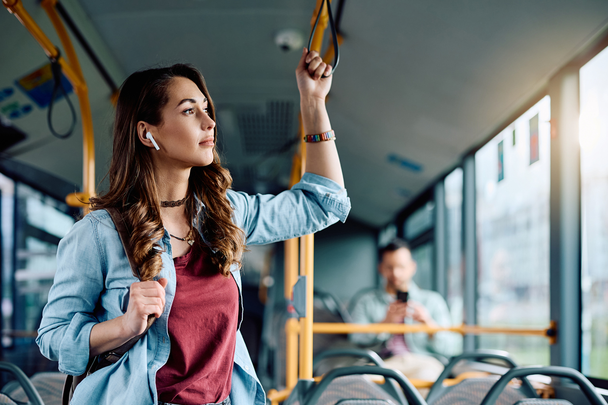 Foto de mulher escutando música em pé em ônibus.